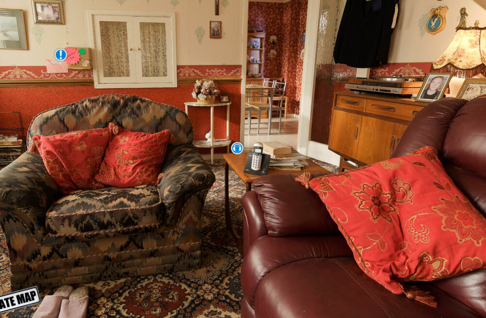 Shameless virtual tour - the living room at Lillian's house. View of a neat but dated living room with sofa and armchair, and view into the kitchen beyond.