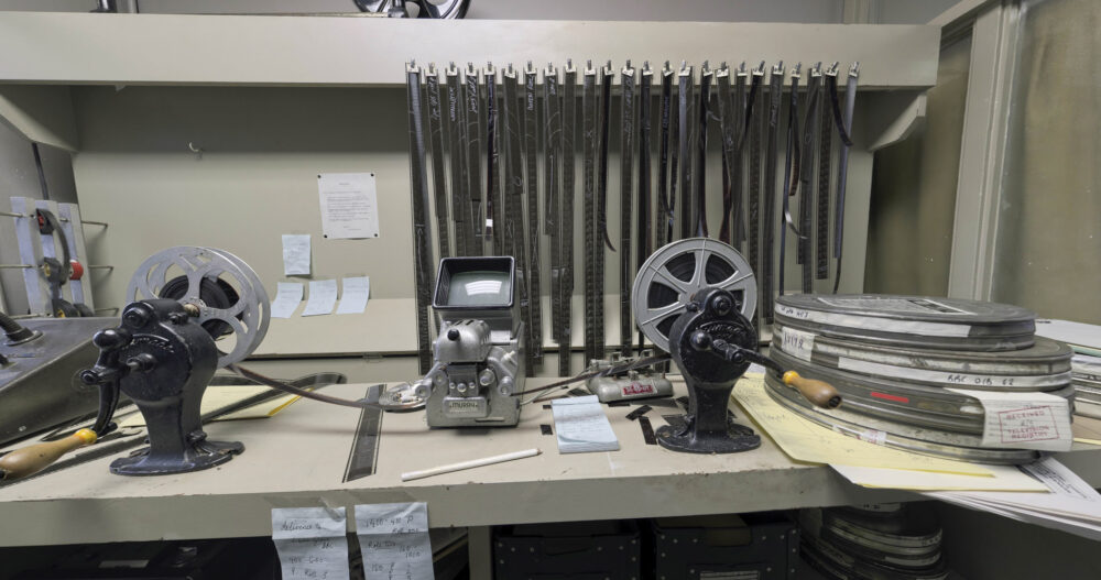 The Hour TV set virtual tour - still from the virtual tour showing the cutting room. Strips of film are seen hanging above a desk with cans of film stacked to the right. On the desk if the machinery used to cut and splice film strips.